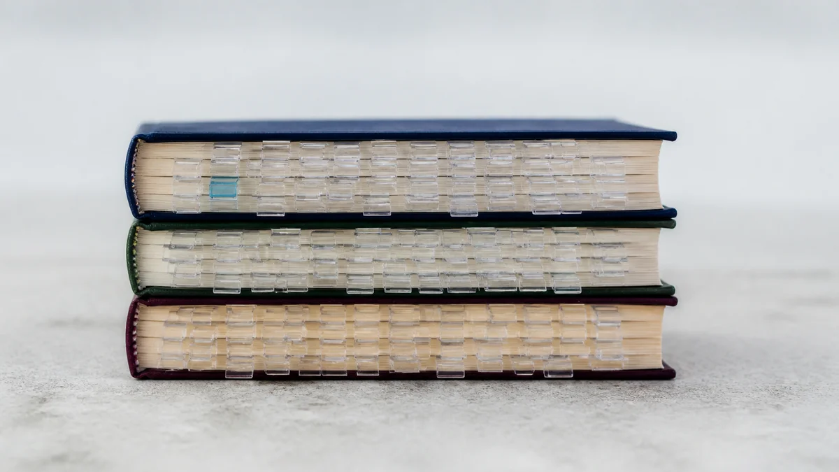 Drei geschlossene Fachbücher mit zahlreichen transparenten Lesezeichenklammern und einem kühlblauen Akzent veranschaulichen, wie neue E-E-A-T-Nachweise die Citation Velocity für KI-Sichtbarkeit erhöhen.