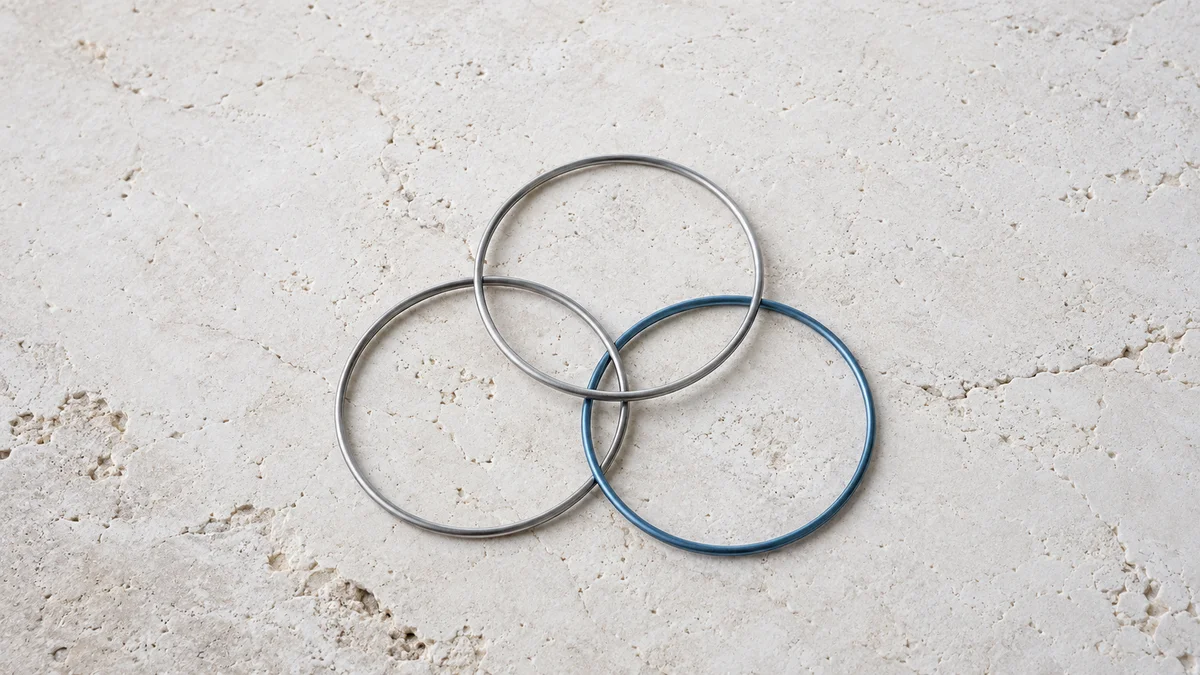 Drei überlappende Metallringe in Silbergrau und Blau auf heller, strukturierter Steinfläche symbolisieren die geringe Überschneidung der Quellen verschiedener KI-Suchmaschinen.
