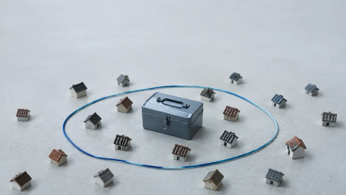 Ein graublauer Werkzeugkasten steht zwischen Miniaturhäusern innerhalb einer blauen Schnur, die das für KI lesbare Einzugsgebiet eines Handwerkers darstellt.
